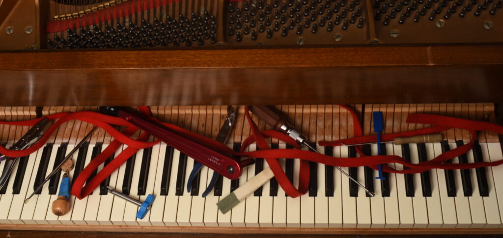 A fun overhead shot of many tools for piano tuning and repair, strewn across the keys of a piano. 